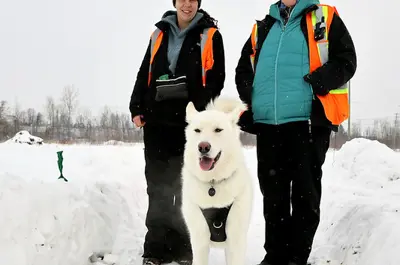 Two women walking a white husky in a snowy field.